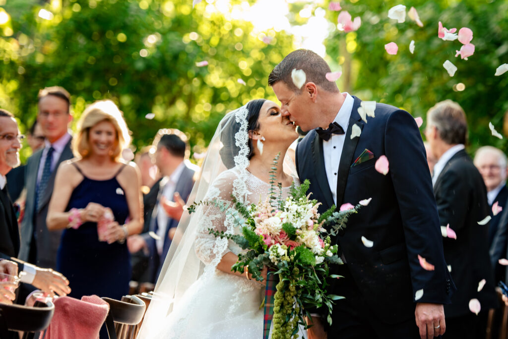 Newlyweds lean in for a kiss during a petal toss.