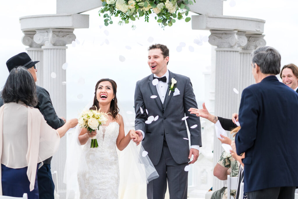 Newlyweds exit their ceremony site showered under a flower petal toss.