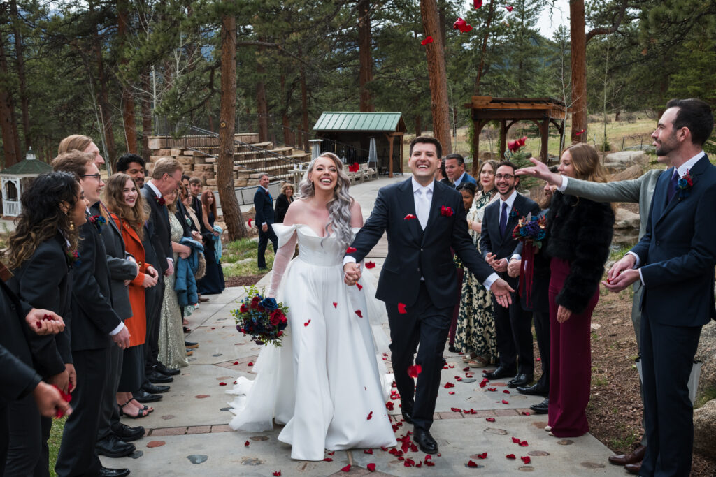Couple walks between tunnel of friends and family for a red petal toss.