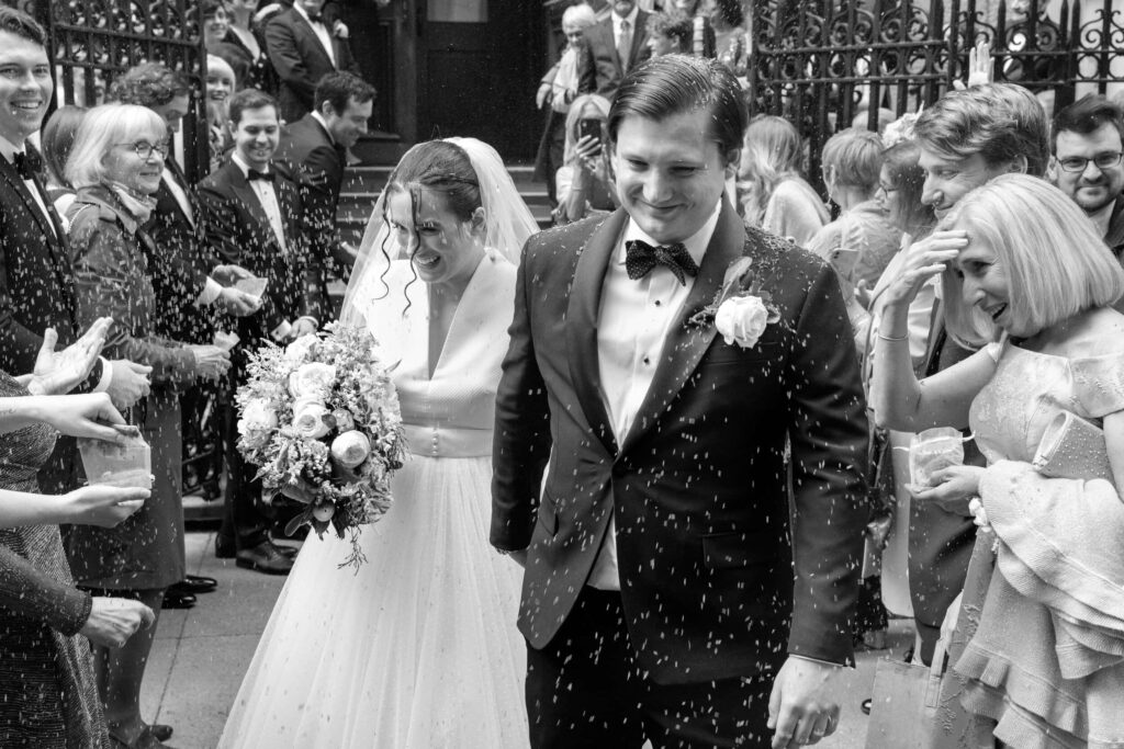 Couple walks out of their wedding venue showered in rice in a classic petal toss exit.