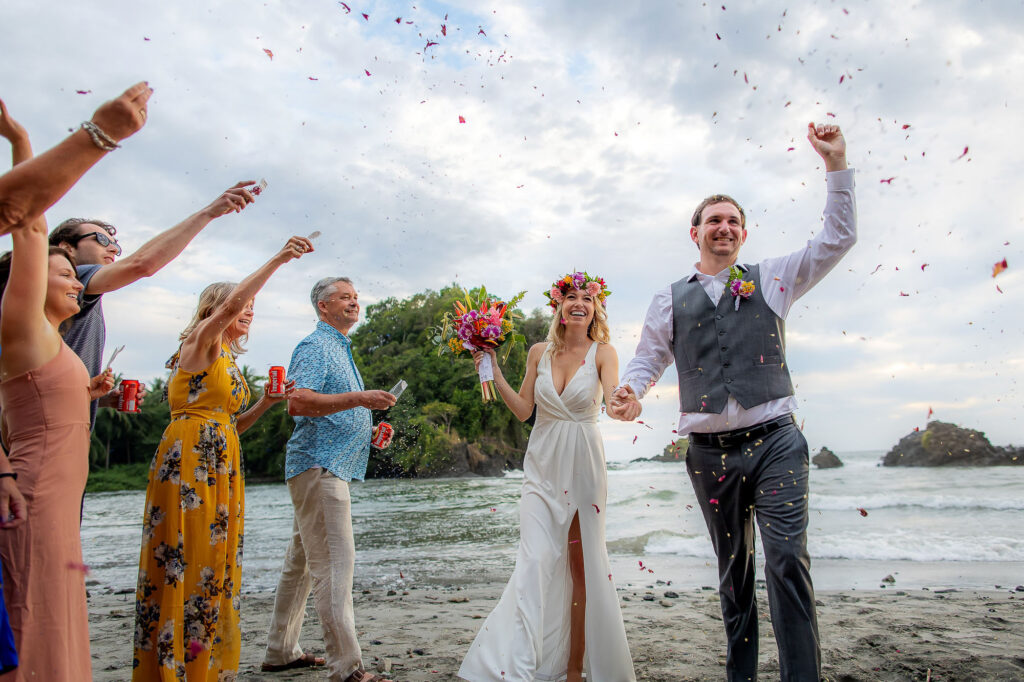 A couple and their family celebrate their marriage with a petal toss on the beach.