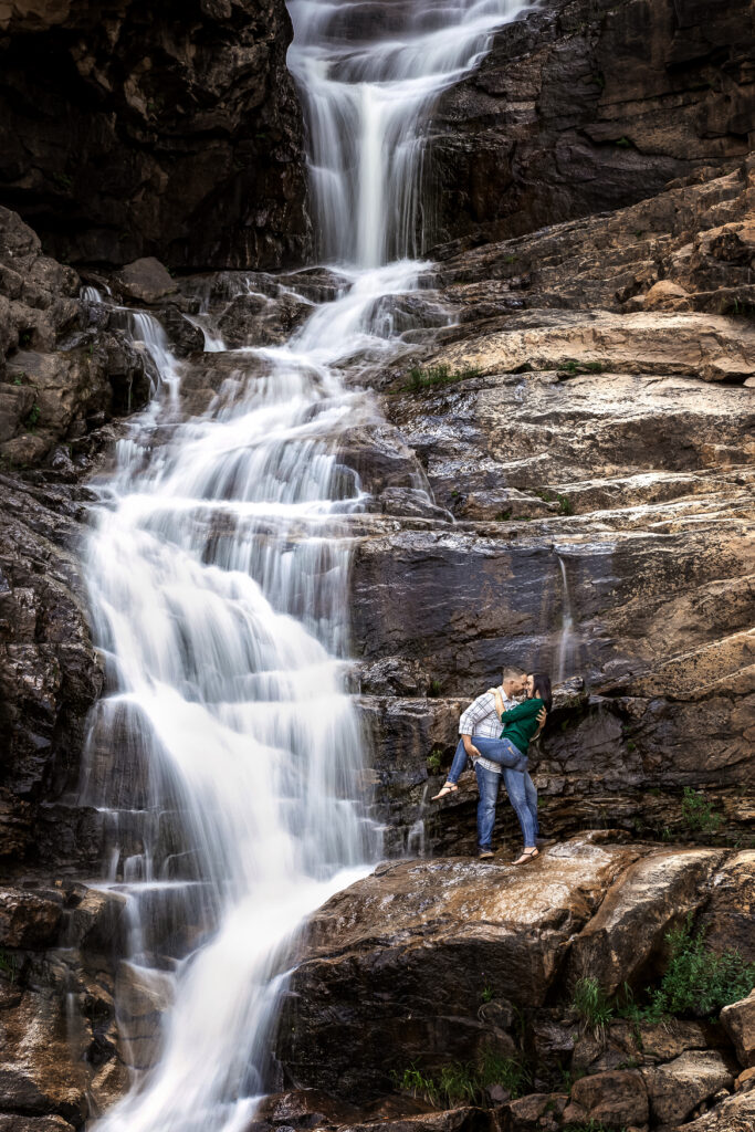 Wedding couple standing still with soft waterfall motion blur behind them by Mot Photography