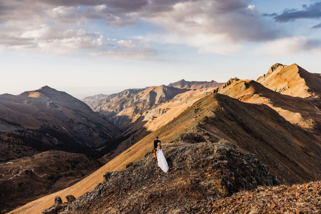 Couple on a rocky ridge with golden light across layered mountains