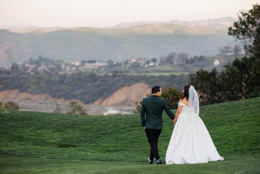 Couple walking down a green slope at a golf club with hills behind them