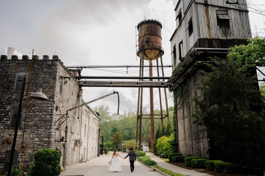 Couple walking down a path between old distillery buildings under a rusted water tower