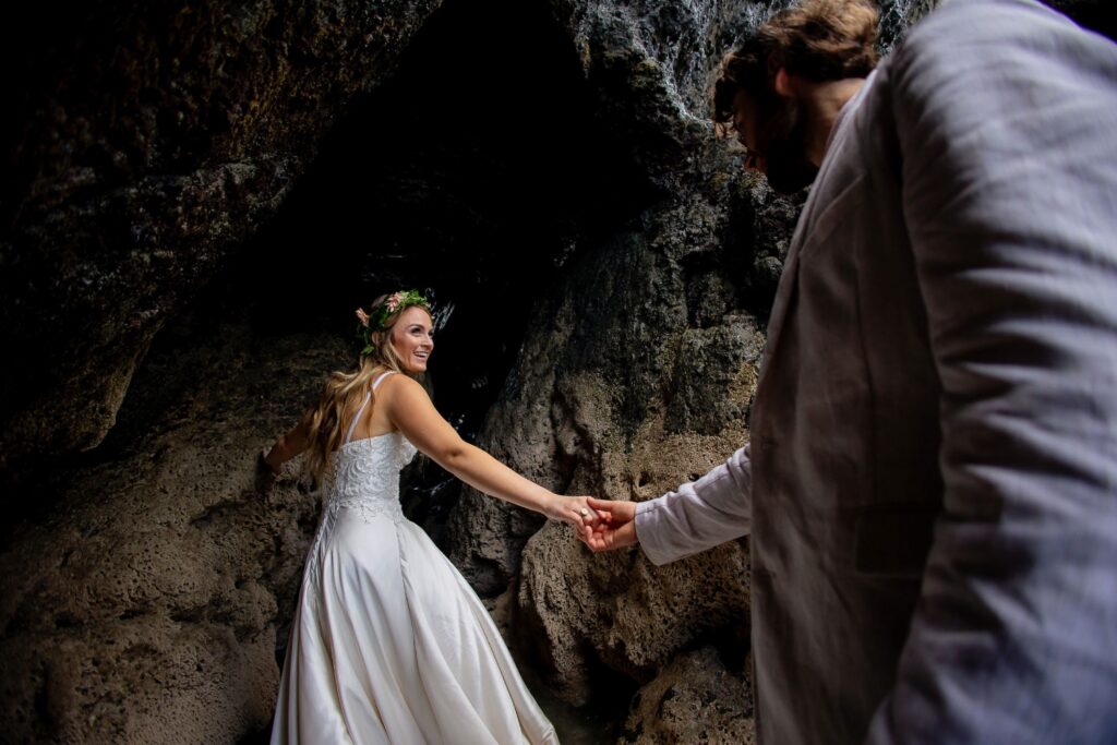 Bride leading the groom by the hand into a rocky cave and looking back