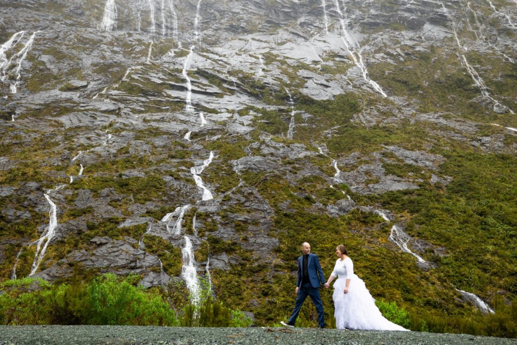 Couple walking past a cliff face streaked with waterfalls