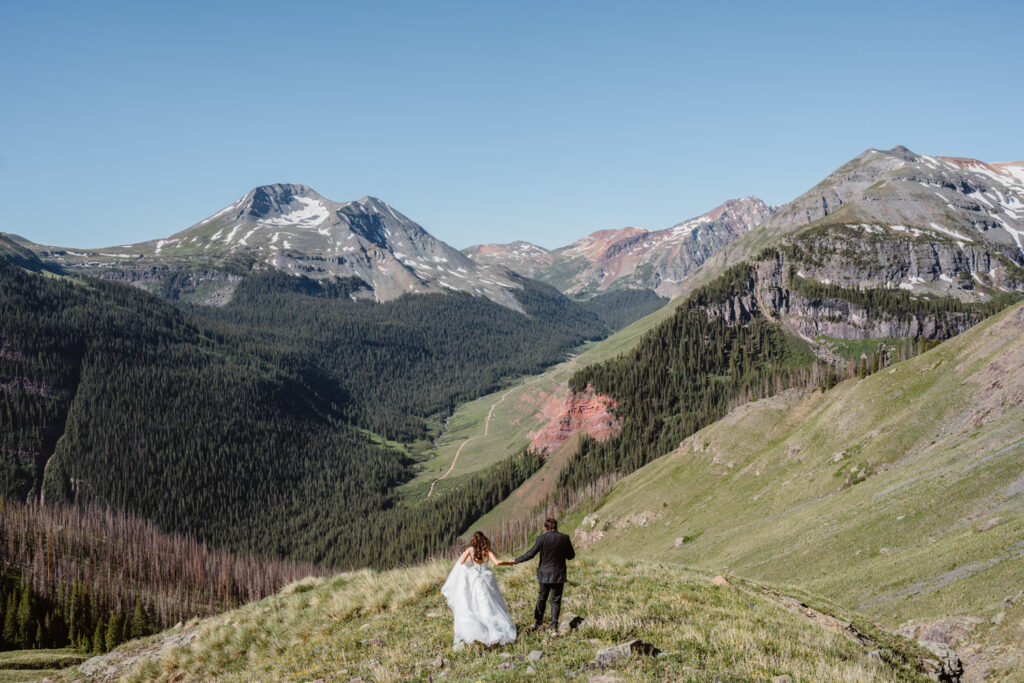 Couple walking away on a grassy slope above a wide mountain valley