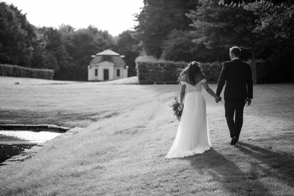 Black and white photo of a couple walking across a lawn toward a garden pavilion